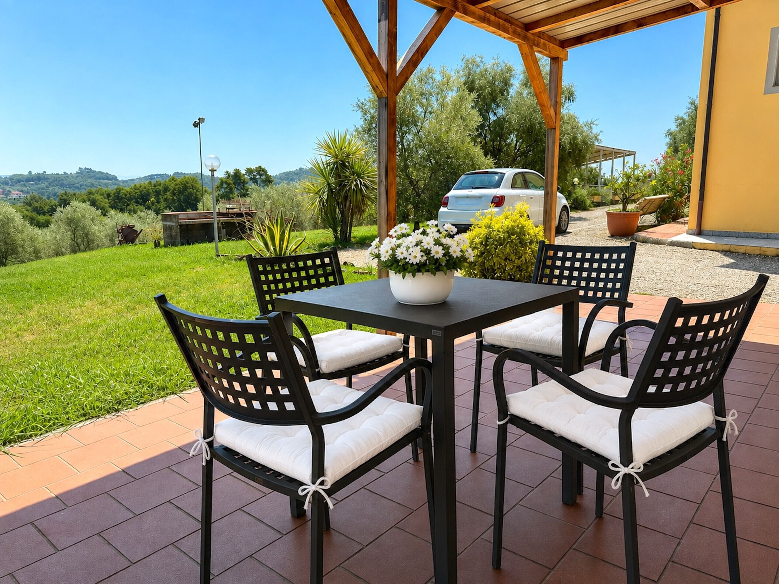 An outdoor patio with a table and chairs, a potted plant, and a view of the surrounding landscape.