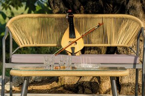 A wicker bench with a glass table in front, a bottle, glasses, and a musical instrument. - Villa Mark (Glossa)