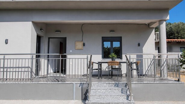 A modern building with a flat roof, a covered outdoor area with a table and chairs, and a staircase leading to an entrance. - Villa Mark (Glossa)