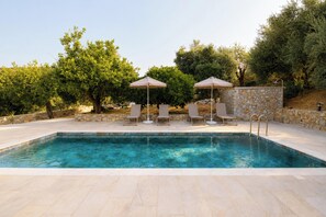 A swimming pool with lounge chairs and umbrellas, surrounded by stone walls and trees. - Villa Mark (Glossa)