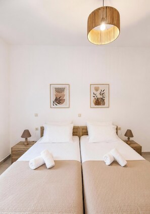 A hotel room with two beds, a hanging light fixture, and two wall-mounted artworks. - Villa Mark (Glossa)