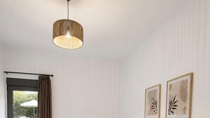 A hotel room with a bed, a bedside table, a lamp, a ceiling light, a window with curtains, and two framed pictures on the wall. - Villa Mark (Glossa)