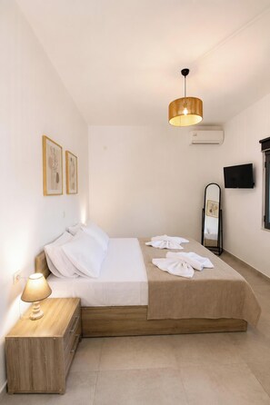 A modern bedroom with a bed, bedside table, lamp, artwork, air conditioning unit, and a TV. - Villa Mark (Glossa)