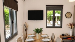 A dining area with a table set for six, a flat-screen TV mounted on the wall, and a clock on the wall. - Villa Mark (Glossa)