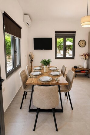 A dining area with a table set for six, a flat-screen TV mounted on the wall, and a clock on the wall. - Villa Mark (Glossa)