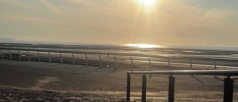 A beach with a metal railing and a clear sky.