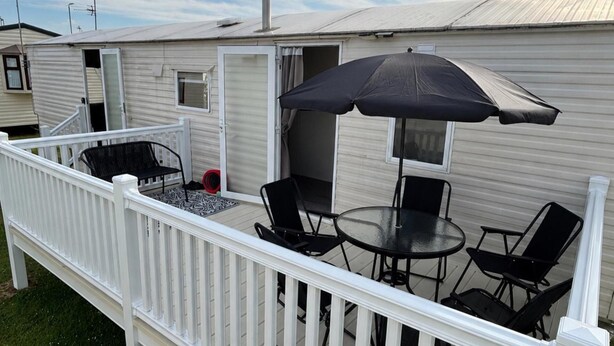 A deck with a table and chairs, an umbrella, and a small window. - Coastal Caravan at Lyons Robin Hood, Rhyl (Rhyl)