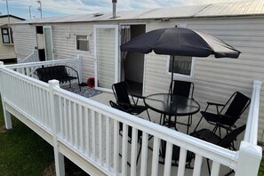 Una terraza con una mesa, sillas, un paraguas y una ventana pequeña.