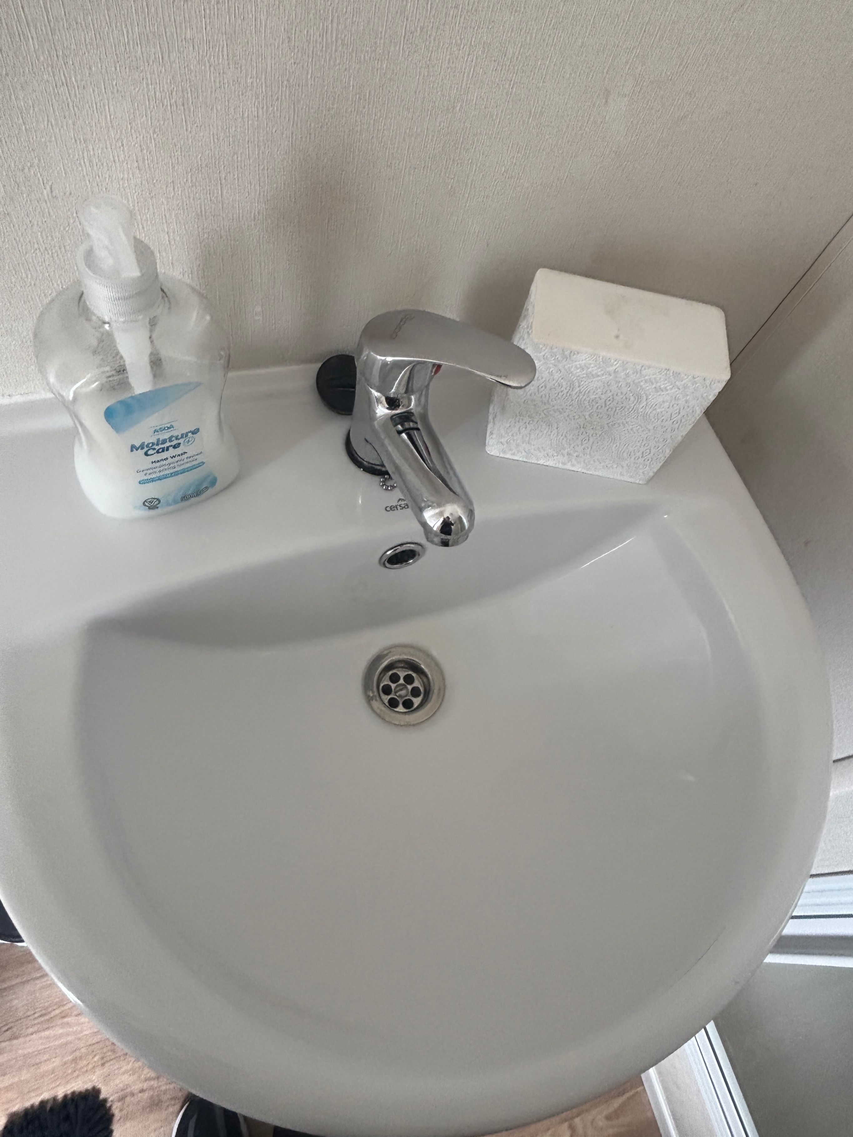 A white bathroom sink with a single faucet, a soap dispenser, and a tissue box.