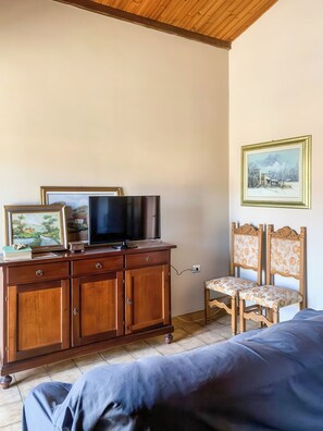 A bedroom with a wooden dresser, a television, two framed pictures, a bed, and a chair. - Casa Paola - Iglesias (Iglesias)