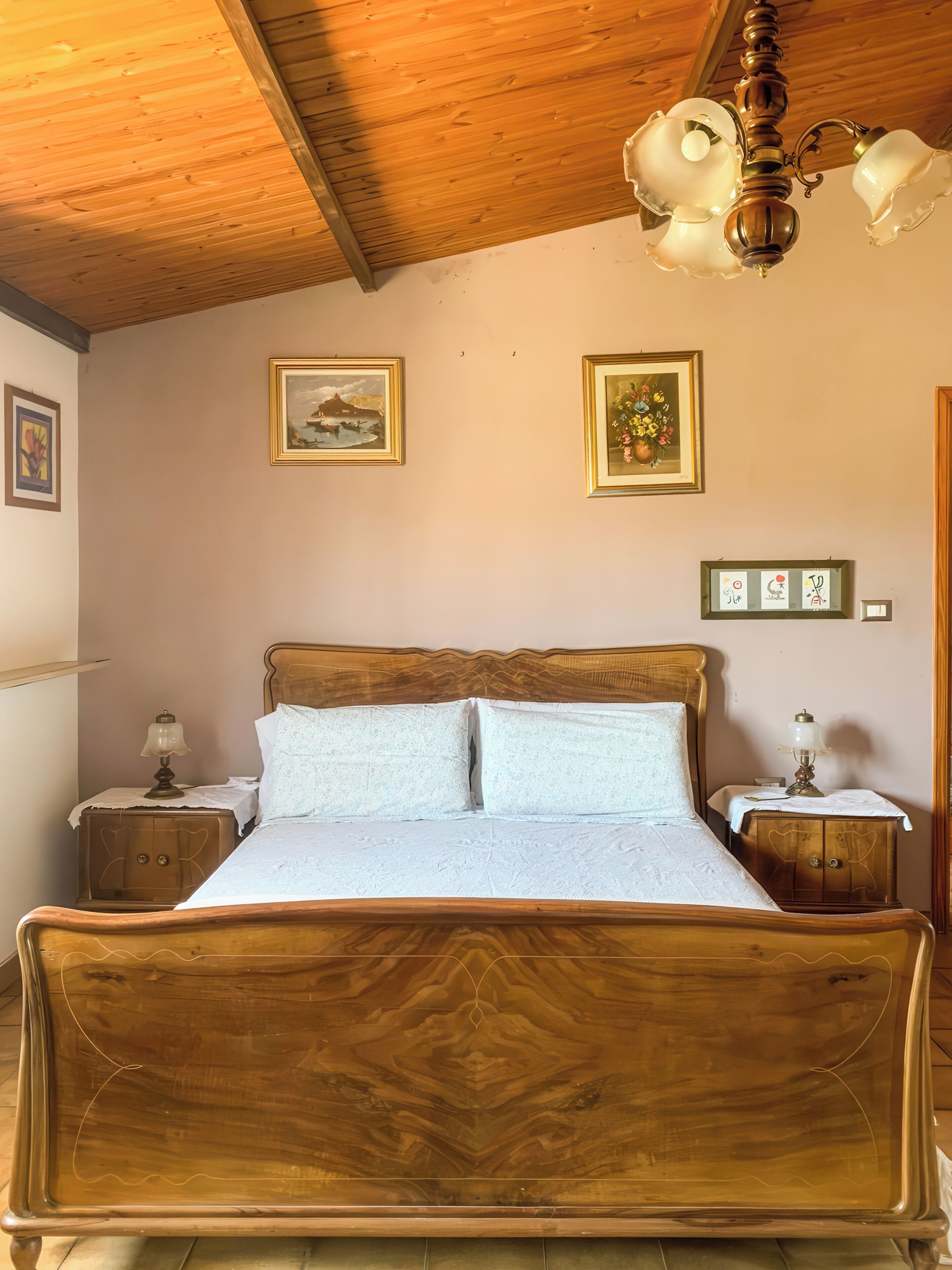 A wooden bed with a headboard, two bedside tables with lamps, and wall-mounted artwork.