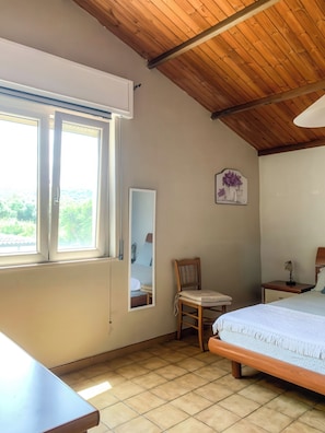 Un dormitorio con techo de madera, una cama, una silla, una mesita de noche, una lámpara, una ventana y un espejo.