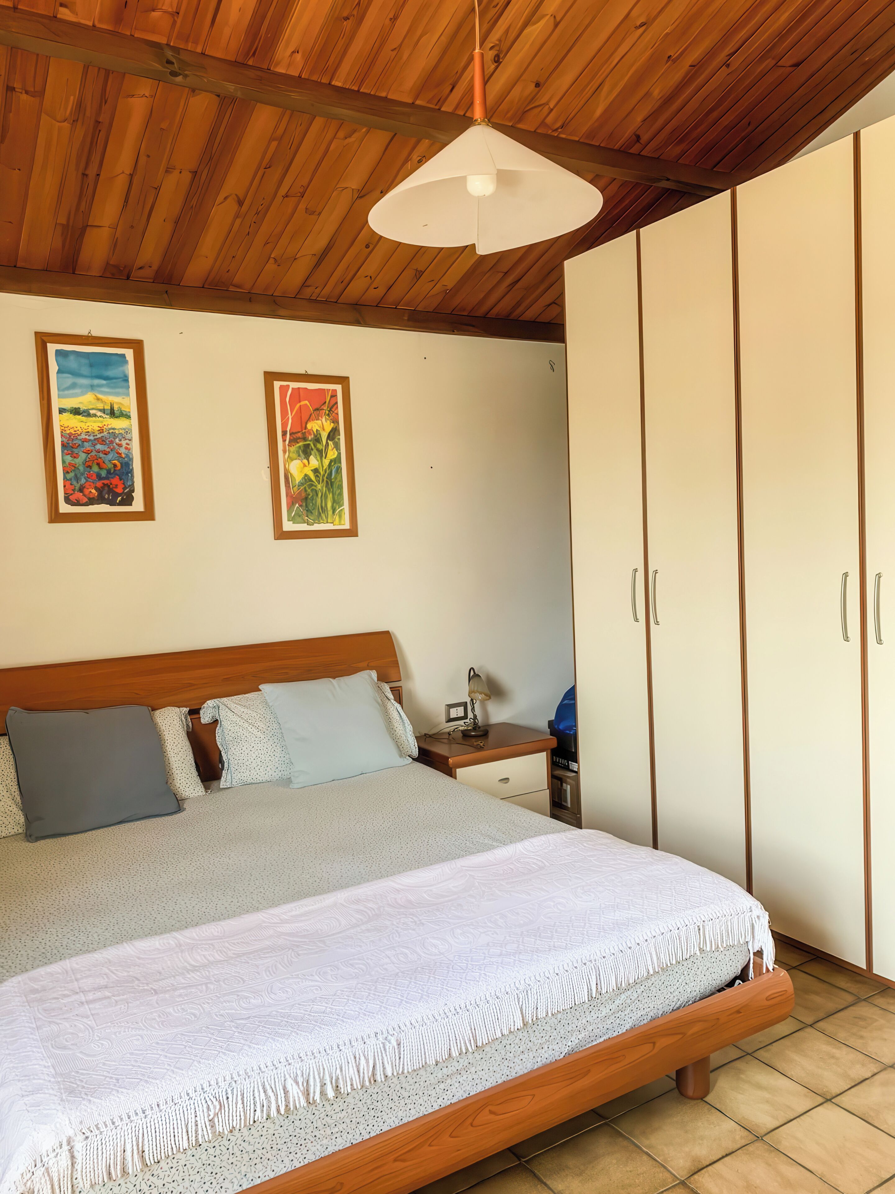 Um quarto com uma cama de madeira, uma mesa de cabeceira, um abajur e um guarda-roupa.