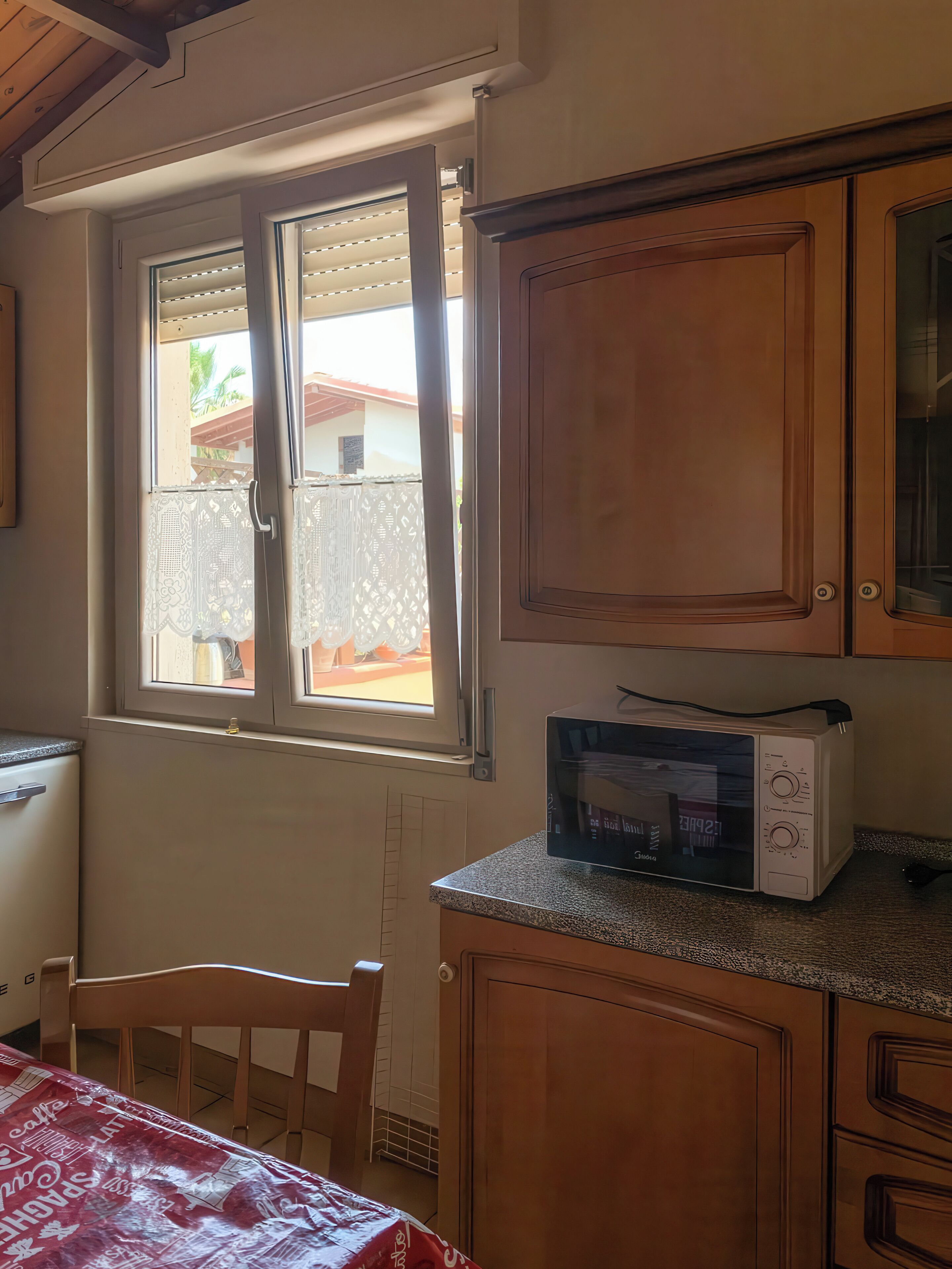 Une cuisine avec des meubles en bois, un four à micro-ondes et une fenêtre avec des stores.