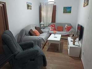 A living room with a sofa, armchair, coffee table, and a flat-screen TV.