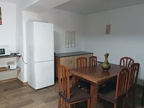 Cocina compacta con nevera, microondas y tostadora sobre una encimera. Hay una mesa de comedor con sillas y un florero.