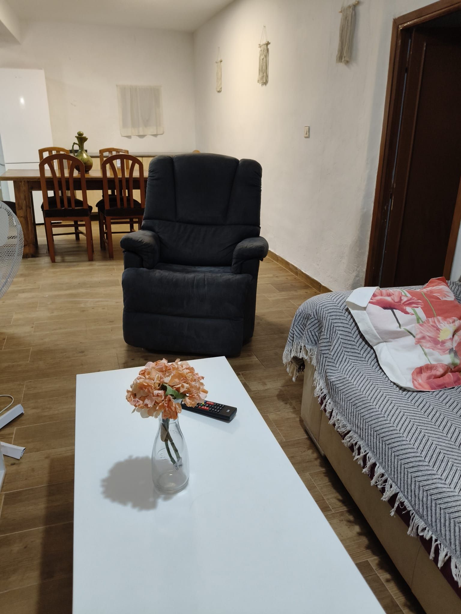 Sala de estar com sofá, mesa de centro com um vaso de flores, controle remoto e cama com cobertor.