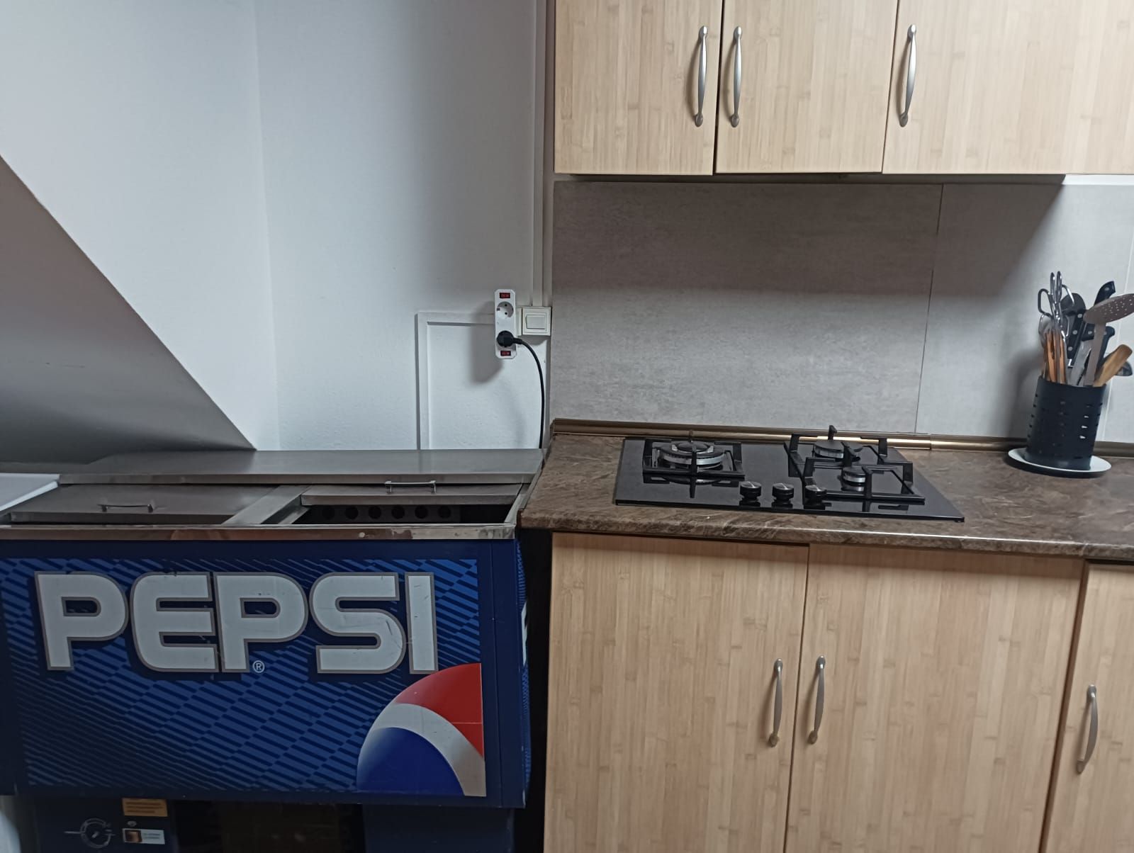 Cozinha com armários de madeira, fogão a gás e geladeira Pepsi.