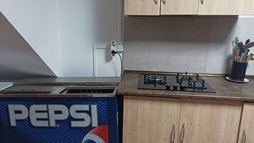 A kitchen with wooden cabinets, a gas stove, and a Pepsi refrigerator.
