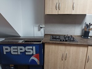 Een keuken met houten kastjes, een gasfornuis en een Pepsi-koelkast.