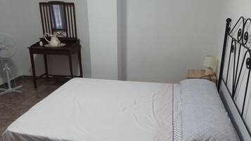 A bedroom with a bed, a bedside table, a chair, a mirror, and a fan.