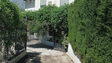 Il s’agit d’une propriété résidentielle avec une allée pavée menant à un bâtiment blanc doté de volets, le tout entouré d’une végétation luxuriante.