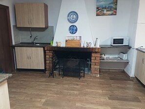 A compact kitchen with wooden cabinets, a brick fireplace, a microwave, and a small shelf. - Bedmar Farmhouse (Bedmar)