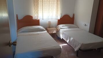 Une chambre avec deux lits simples, une table de chevet avec une lampe, une fenêtre avec des rideaux en dentelle et une porte avec une poignée en laiton.