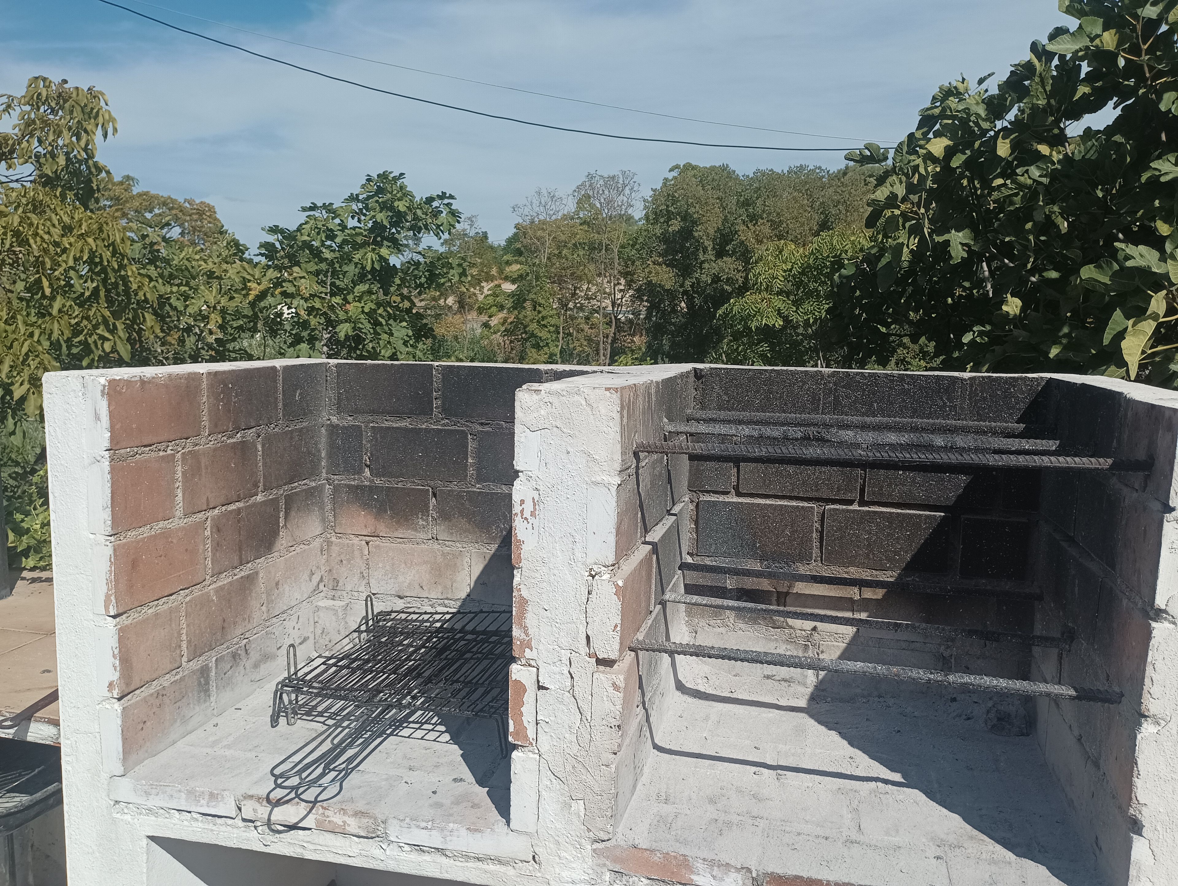 Un barbecue en briques avec une grille en métal, entouré de verdure.