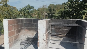 Un barbecue en briques avec une grille en métal, entouré de verdure.