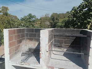 Churrasqueira de tijolos com grade de metal, cercada por vegetação.
