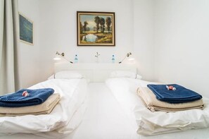 A hotel room with two beds, a painting on the wall, and a bedside table with a lamp and water bottles.