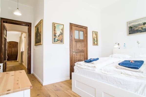 A bedroom with a wooden door, a bed with white bedding, and a painting on the wall.