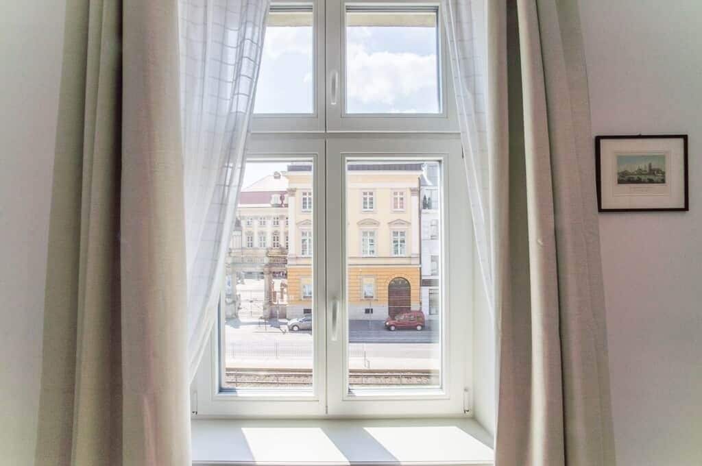 A room with a large window, curtains, and a framed picture on the wall.
