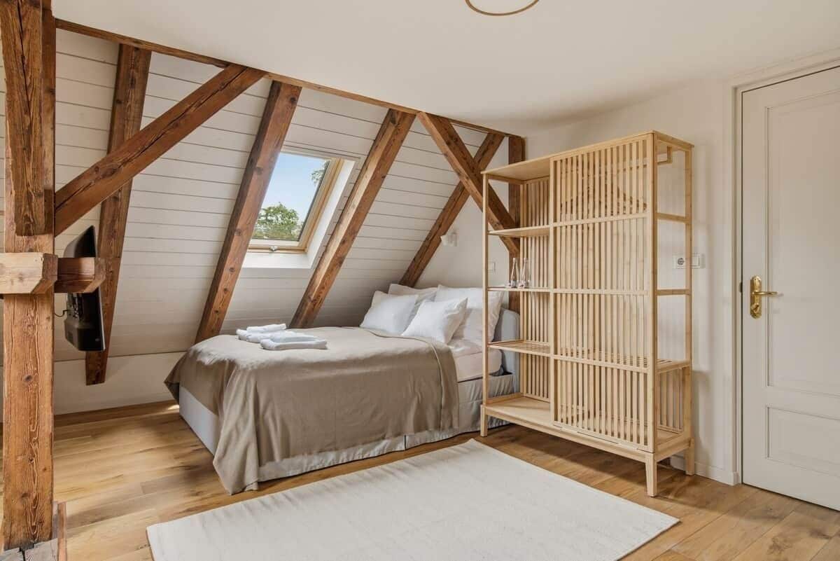 Een slaapkamer met een schuine kap, een bed met een beige dekbed, een houten kinderbedje en een witte deur.