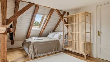 Een slaapkamer met een schuine kap, een bed met een beige dekbed, een houten kinderbedje en een witte deur.