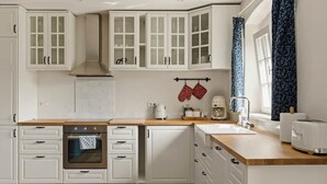 A kitchen with white cabinetry, a wooden countertop, a stove, and a window with a curtain.