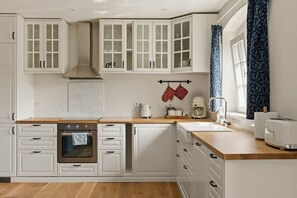 A kitchen with white cabinetry, a wooden countertop, a stove, and a window with a curtain.