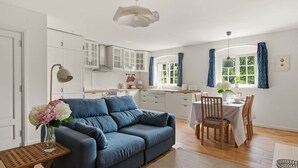 A modern kitchen with white cabinets, a dining area with a table set for two, and a blue sofa in the living area.