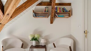 A room with two white chairs, a small table with a vase of flowers, and two wooden bookshelves with books.