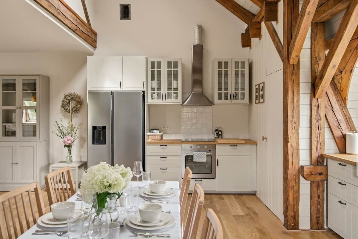 A modern kitchen with white cabinetry, a stainless steel refrigerator, and a wooden ceiling.