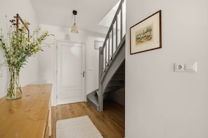 A hallway with a wooden floor, a white door, a staircase with grey railings, and a framed picture on the wall.