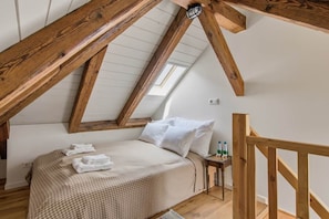 A bedroom with a sloped ceiling, a bed with a checkered bedspread, white pillows, and a nightstand with bottles.