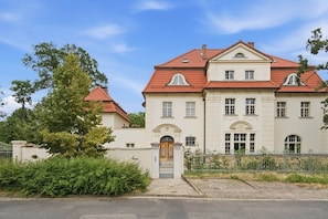 Ein großes, zweistöckiges Geb äude mit einer symmetrischen Fassade, einem zentralen Eingang mit einem dekorativen Bogen und einem roten Ziegeldach.