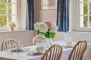 A dining table set for four with a vase of flowers, white tablecloth, and blue patterned curtains. - Villa Meinecke - Apartment 4 'Zoo' (Wrocław)