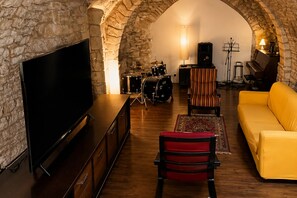 Ein gemütliches Wohnzimmer mit Fernseher, Schlagzeug, Klavier und einem gelben Sofa.