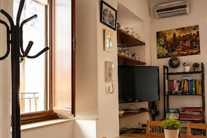 A room with a television, bookshelves, a coat rack, and a window with a view. - Charming Apartment Near Bari & Alberobello (Bitritto)