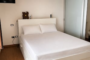 A single-bed room with a white headboard, a bedside table with a lamp, and a wall-mounted light fixture. - Charming Apartment Near Bari & Alberobello (Bitritto)