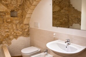 Ein Badezimmer mit Steinwand, Toilette und Waschbecken in Weiß, darüber ein Spiegel.