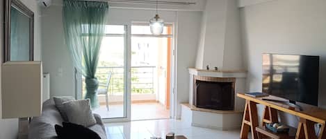 Una sala de estar con sofá, televisión, chimenea y puerta corrediza de vidrio que da a un balcón.